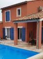 Two-story Mediterranean-style house with red tile roof, blue shutters, and a swimming pool in the backyard. The house has a covered patio area with outdoor furniture.
