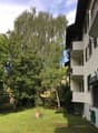Building with balconies, grassy lawn, several trees, wooden bench, metal railings