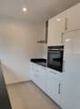 modern kitchen with white cabinets, black countertops, stainless steel sink, built-in oven and dishwasher, windows