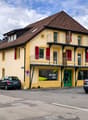 yellow house, brown roof, red shutters, balcony, parking place
