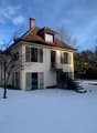 white exterior, brown roof, chimney, stairs leading to front door, snow-covered ground, two-story, multiple windows