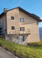 detached 3 story house with raised ground floor, green landscape, driveway, lake and mountain view
