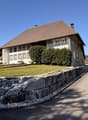 2 story house, brown roof, white walls, multiple windows, stone wall, driveway, green lawn, trees