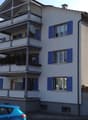 Four story building, white exterior, blue shutters, balconies, chimney, parking in front