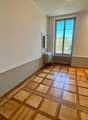 Empty room with wooden parquet flooring, white walls, a window, a small sink, and a radiator.