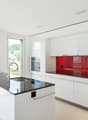 Modern, open-concept kitchen with white cabinets, red glass backsplash, and a large island with a black granite countertop. The kitchen features built-in appliances, including a dishwasher.