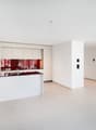 Modern, open-concept kitchen with white cabinets, black countertops, and a red glass backsplash. The kitchen is integrated into the living space and has a clean, minimalist design.
