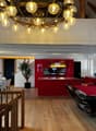 The image shows a large, open-concept living space with a dining area, kitchen, and entertainment area. The space features a high, vaulted ceiling with a large, ornate chandelier. The walls are a mix of white and red, with wooden beams and accents. The ki