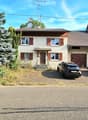 Detached house, two storeys, brown roof, white walls, wooden door, brown garage doors, trees, parking for two cars.
