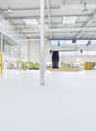 Large open commercial space with high ceilings, white walls, and yellow accents. The space has a stage-like area and appears to be a multipurpose event or exhibition hall.