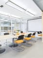 Modern office space with large conference table, swivel chairs, projector screen, and glass walls providing natural light
