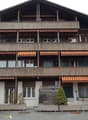 3-story wooden chalet-style building with balconies, decorative wooden trim, and awnings