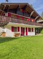 2 story chalet, wooden balcony, red shutters, white walls, wooden bench, wooden storage box, well-maintained lawn