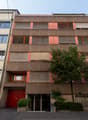 4 story building, red doors, multiple windows, beige and brown exterior, tree in front