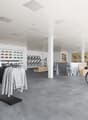 Large open space with clothing racks, shelves displaying accessories, and bicycles on display. The space has a modern, minimalist design with white walls, gray flooring, and recessed lighting.