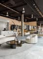 Large open space with concrete floors, black ceiling with track lighting, display racks and shelves for clothing, a curved white sofa and coffee table in the center, and a reception desk at the back of the store.