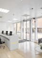 modern office with white walls, beige tiles, large windows, reception desk, office chairs, couch, coffee table, flower vase