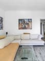 L-shaped sofa, glass coffee table, two paintings on the wall, TV, remote control on the table, white curtains