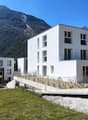 White apartment building, modern design, concrete driveway, green lawn, mountains in the background