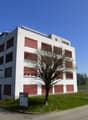 Building: multiple windows, red doors, signboard, grassy area, street
