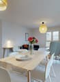Dining room with a table, chairs, and a flower vase on the table. There is a lamp on the wall and a plant in the corner. The room has a sliding glass door leading to a balcony.