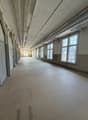 Empty room with white walls, ceiling, and floor, large windows, and doors on the left side