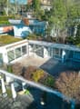 Modern house with a rooftop terrace, surrounded by trees and plants, open patio with outdoor furniture, multiple windows.