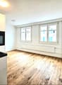 Empty room with wooden floor, white walls, two windows, built-in oven, and a sink.
