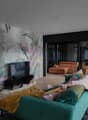 living room with large glass windows and balcony, wooden floor, teal sofa with cushions, coffee table, and wall mural, TV, and a rug