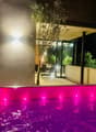 Jacuzzi with pink water and purple lights at night, next to an olive tree, with a dining area and a balcony behind