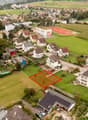Suburban neighborhood with various sized houses, one empty plot marked with red rectangle, houses have various features like garages and solar panels