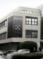 4-story office building with a modern, glass and concrete facade. The building is located on Rue de la Pierre à Mazel 39 in Neuchâtel, Switzerland and is part of the Innoparc 4 complex. There are several cars parked in front of the building.