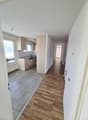 Empty hallway with wooden floor, white walls, kitchen with sink, cabinets, and dishwasher