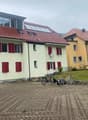 Two-story house with red roofs and windows, solar panels, brick driveway, bicycles parked