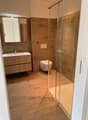 Bathroom with wooden floor, glass shower, wooden vanity, toilet, mirror