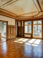 large room, wooden parquet flooring, wooden paneling, wooden ceiling with intricate design, double doors, windows with grills
