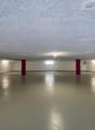 Large open space with concrete floor, white walls, and red columns. The room appears to be a basement or garage area with overhead lighting.