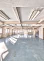 large open space, white walls and ceiling, windows, overhead lighting, radiators, clean