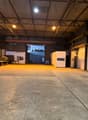 large warehouse with high ceilings, open space, brick walls, metal racks, 2 white doors, a truck with trailer parked at the entrance, steel door at the end of the room