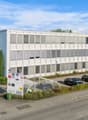 white office building with multiple windows, two stories, entrance, shrubs, parking area, bicycles parked under canopy