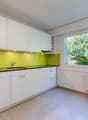 modern kitchen with white cabinets, yellow backsplash, granite countertop, stainless steel sink, faucet, large window with view of trees