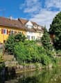 two-story house, yellow exterior, brown roof, red shutters, garden with stairs leading to river