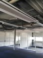Large open space with office walls and glass doors, metal ceiling with overhead pipes and lighting