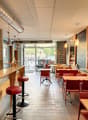 a restaurant with a bar counter, several tables, chairs, red leather stools, lamps, menu boards, a framed picture on the wall, a blackboard, and a glass door leading to the outside