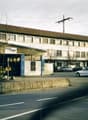 A building with several windows, parked cars in front, street light pole, road.