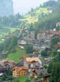 Mountain village with many houses, green hills, trees, and a mountain in the background