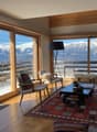 large glass windows, wooden floor, carpet, glass door to balcony, coffee table, chairs, statue, rug, mountains view