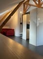 Exposed wooden beams, red couch, grey carpet, white kitchen, lamp, ceiling lamp, wooden table