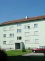 3 story apartment building, green exterior, brown roof, multiple windows, cars parked in front