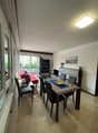 open space living room with large windows, balcony access, dining table, sofa, TV stand, floor lamp